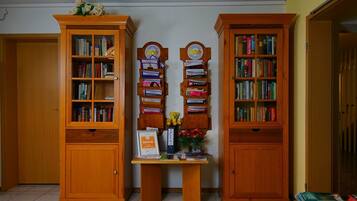 Une pièce avec deux étagères en bois remplies de livres, une petite table sur laquelle est posé un vase de fleurs, et une enseigne indiquant « hotel.de ».