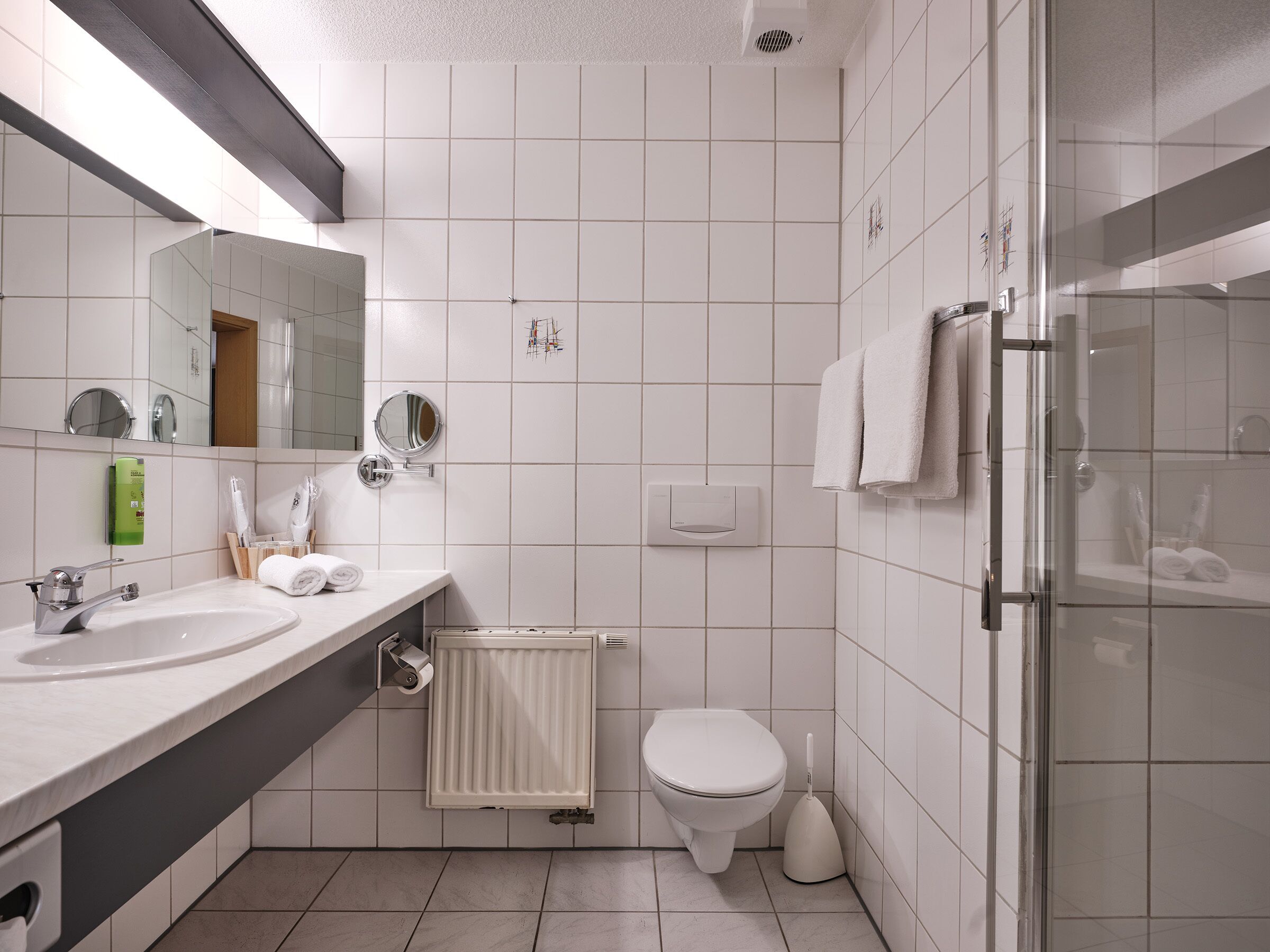 Un baño moderno con lavamanos, espejo, inodoro y ducha.