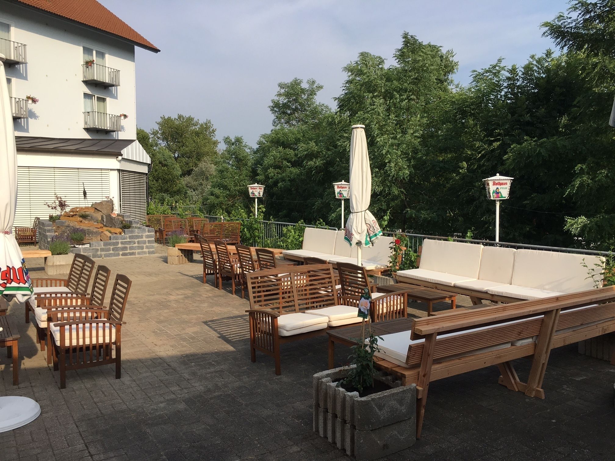 Eine Außenpatio-Terrasse mit Holzmöbeln, darunter Tische und Stühle, sowie ein Steingartenbeet mit einer Pflanze.