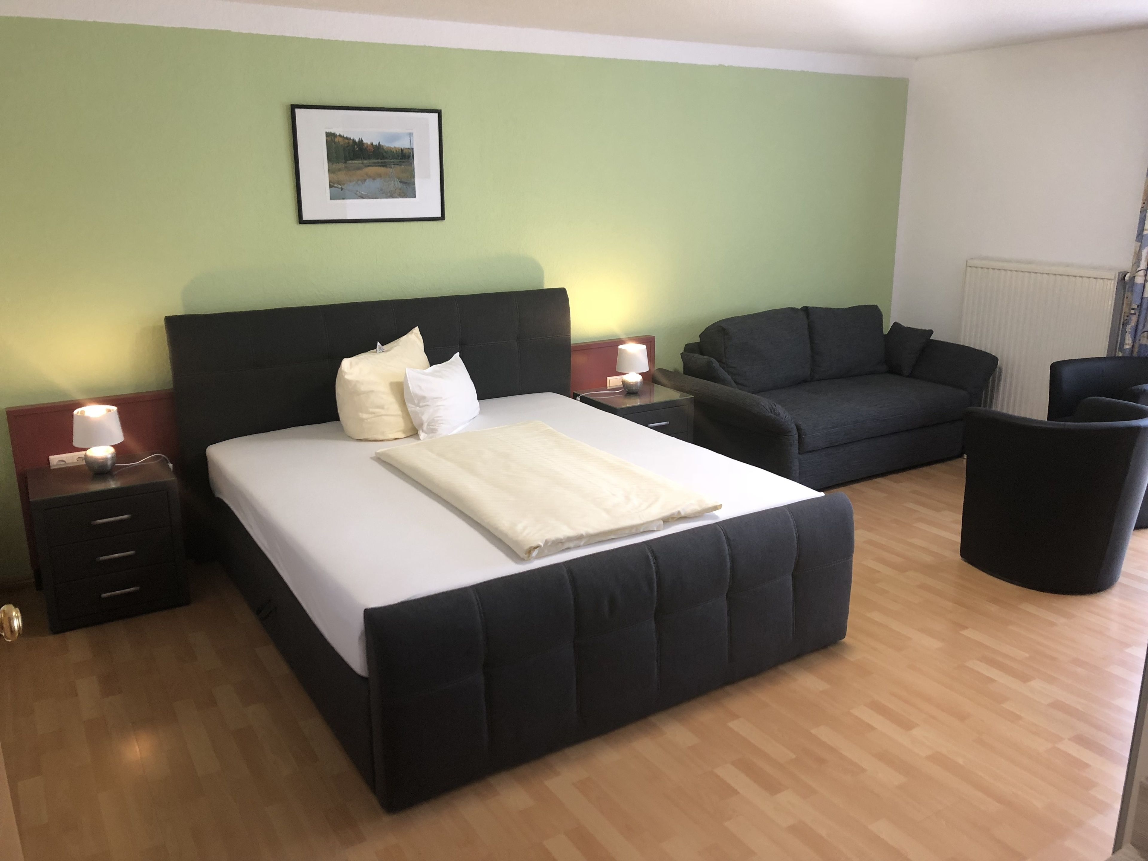 Une chambre d’hôtel avec un grand lit, un canapé, un fauteuil et une petite table avec une lampe.