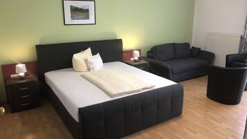 Une chambre d’hôtel avec un grand lit, un canapé, un fauteuil et une petite table avec une lampe.