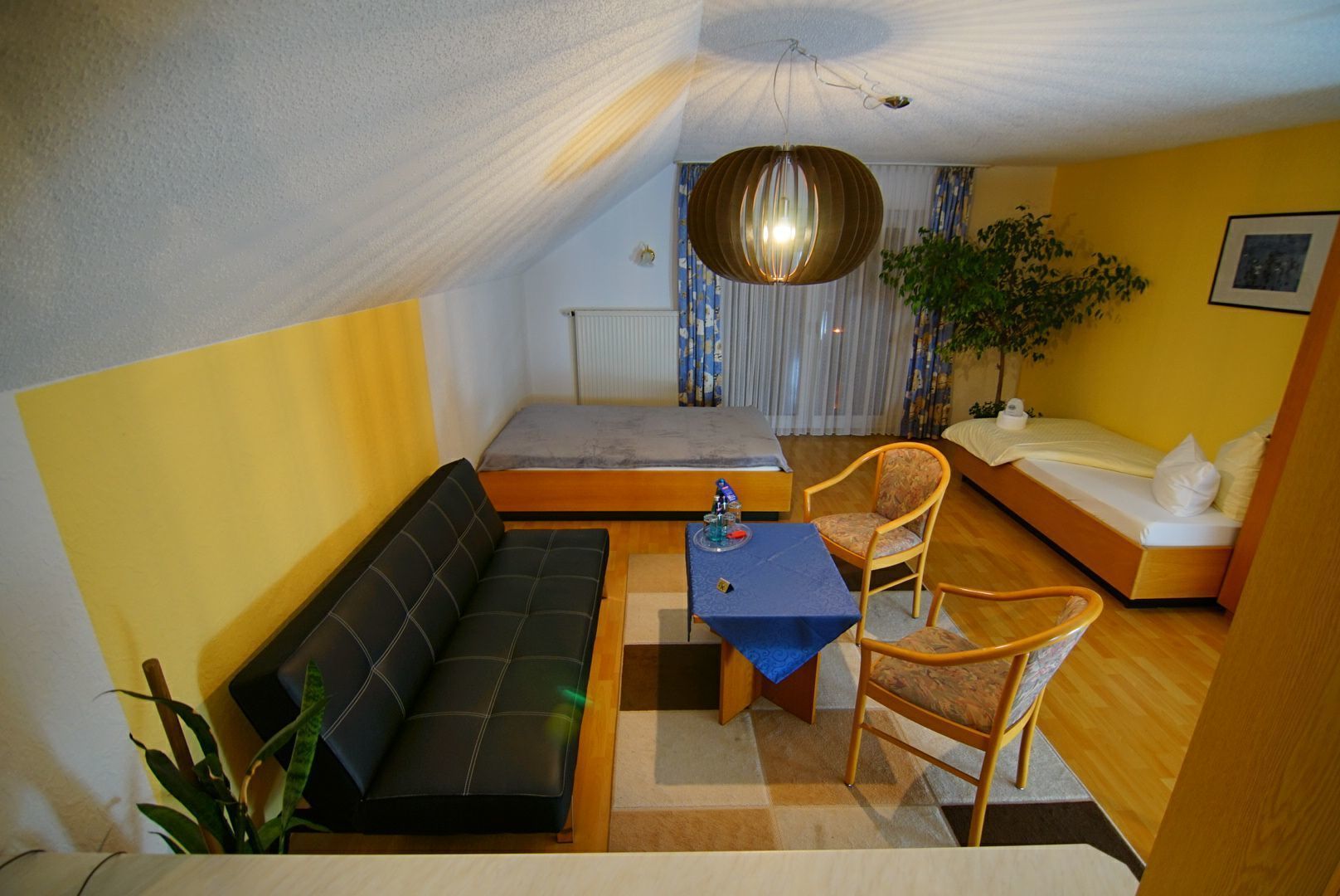 A compact hotel room with a sofa, a small table, a chair, and a bed.