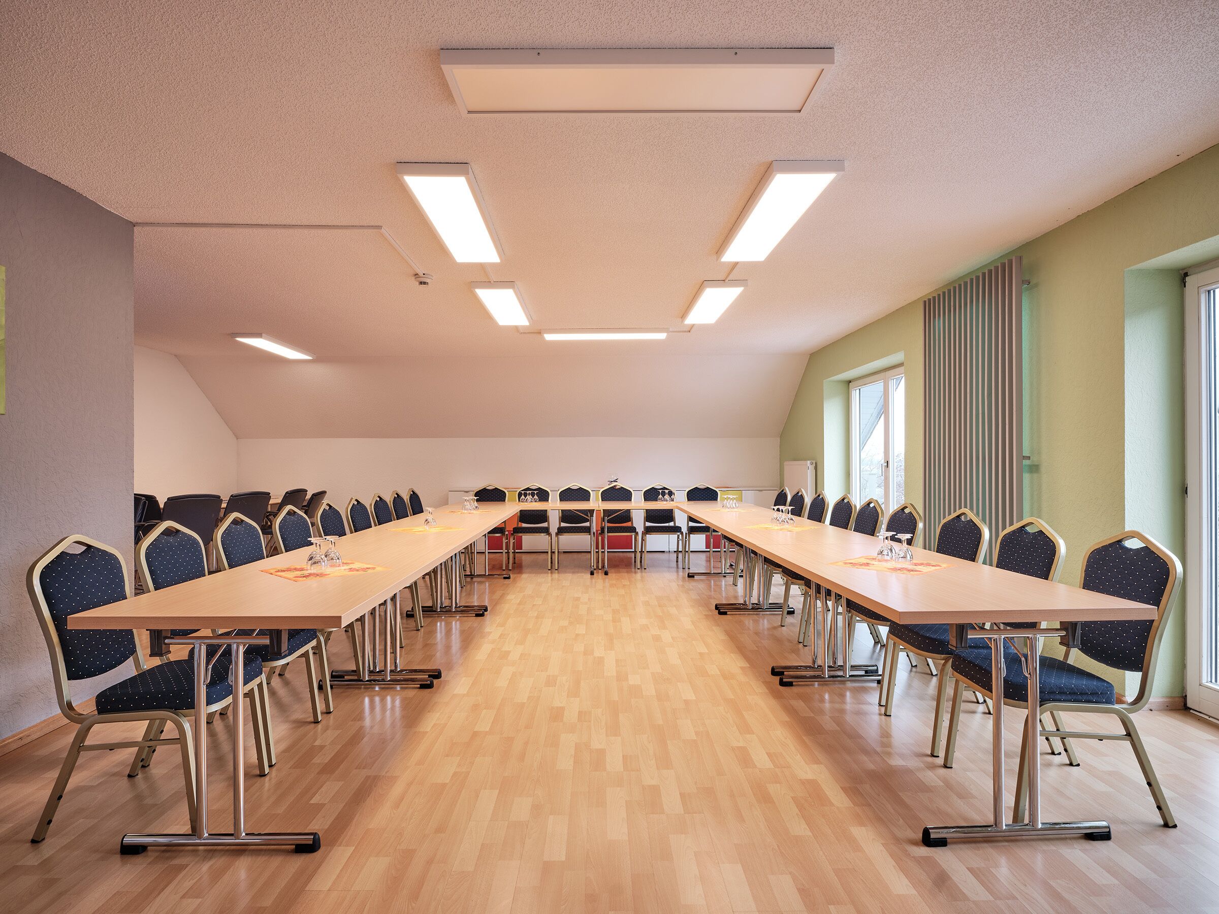 Ein Konferenzraum mit langem Tisch, Stühlen, Holzboden und Deckenleuchten.