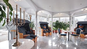 A spacious indoor area with a high ceiling, large windows, and a polished marble floor. There are several seating areas with cushioned chairs and tables, and a variety of potted plants. - Hotel am Hochrhein (Bad Saeckingen)