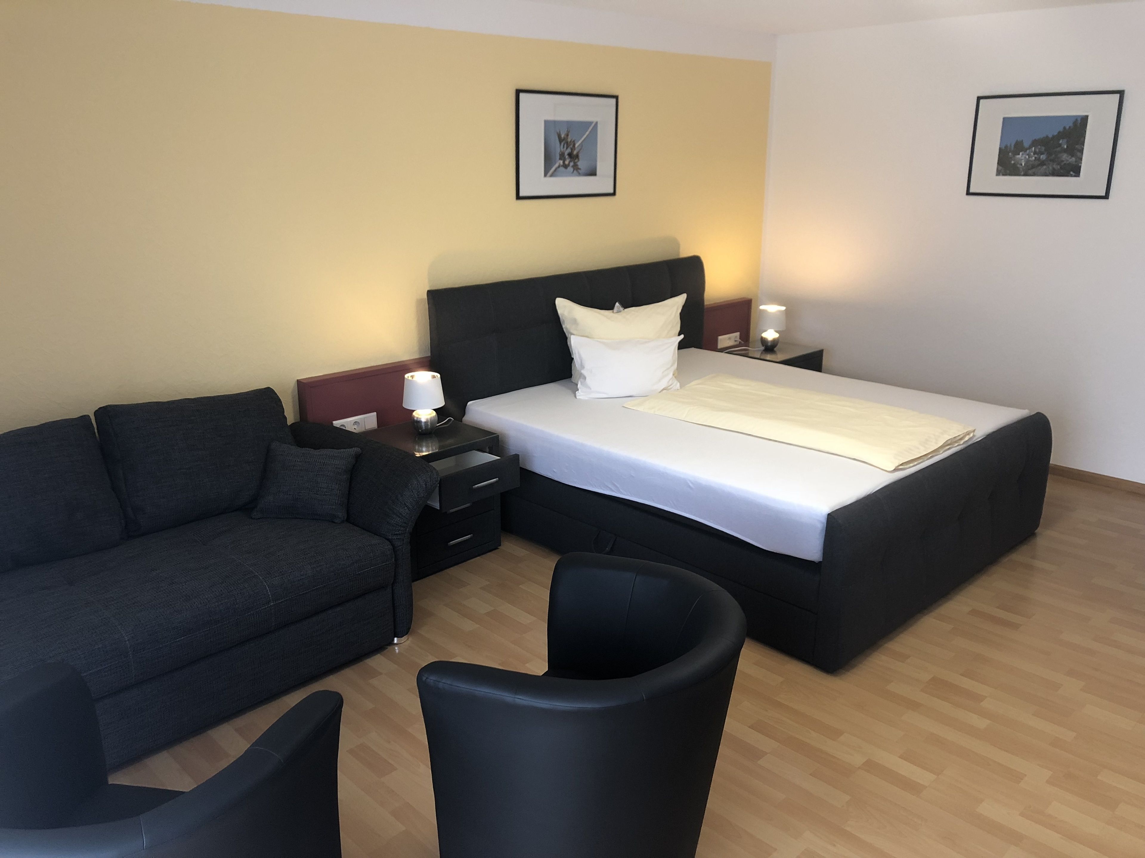Una habitación de hotel con una cama, un sofá, un sillón y dos mesitas de noche con lámparas.