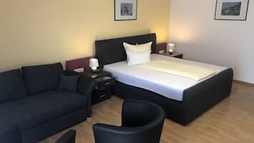 Una habitación de hotel con una cama, un sofá, un sillón y dos mesitas de noche con lámparas.