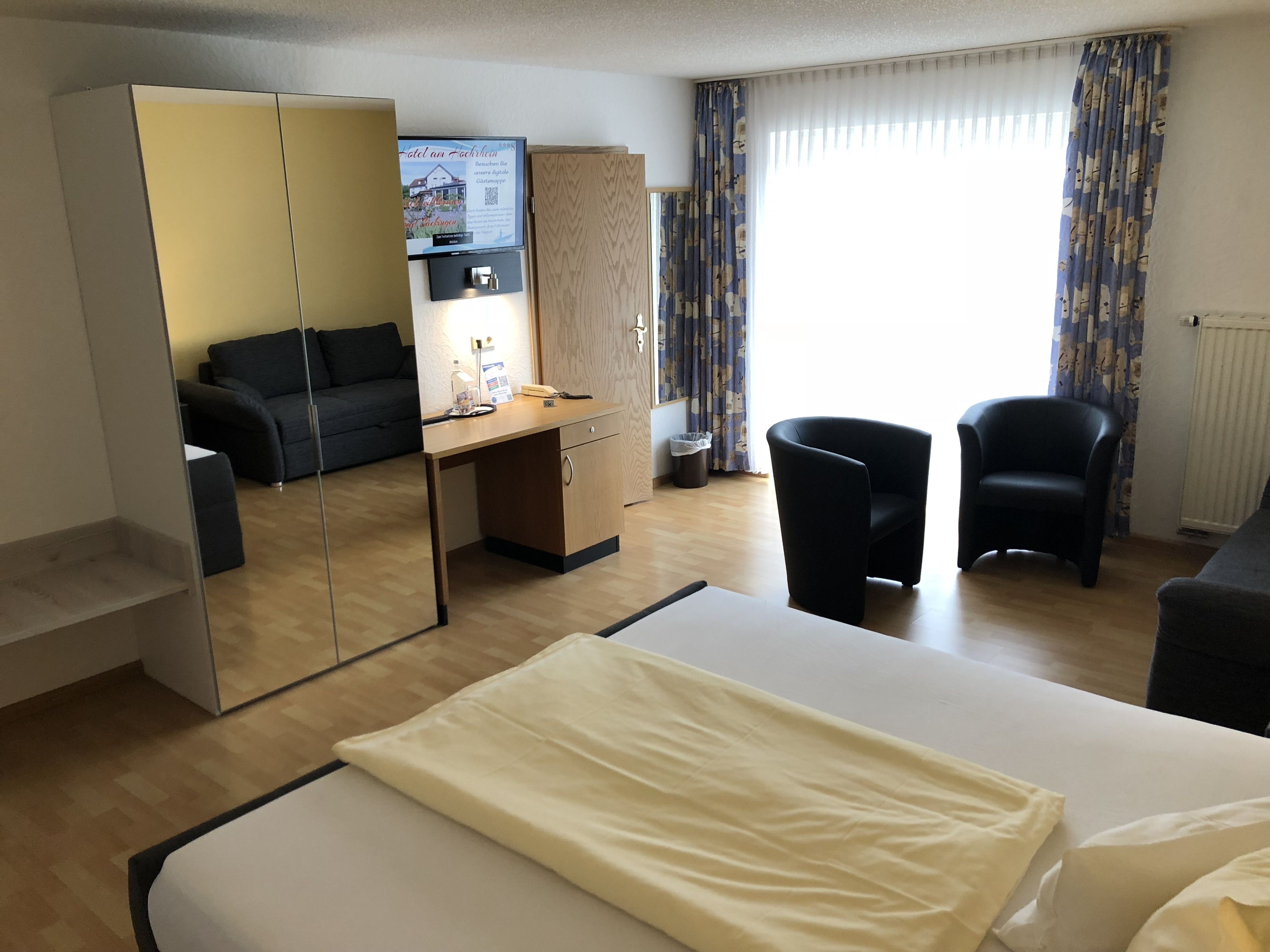 Una camera d'albergo con un letto, una scrivania, una sedia, un divano e un armadio.