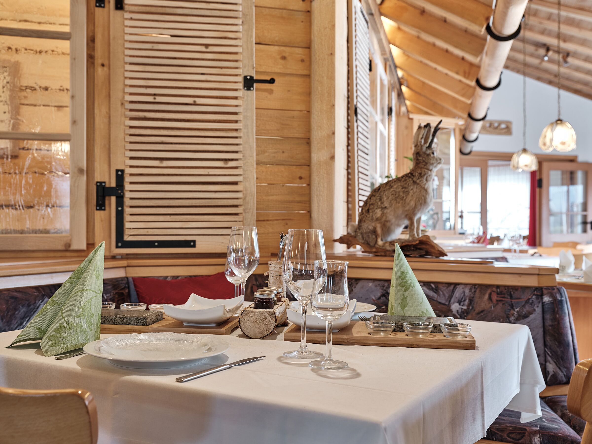 Interior de restaurante con paredes de madera, una mesa preparada para comer y una figurita de conejo en la barra.