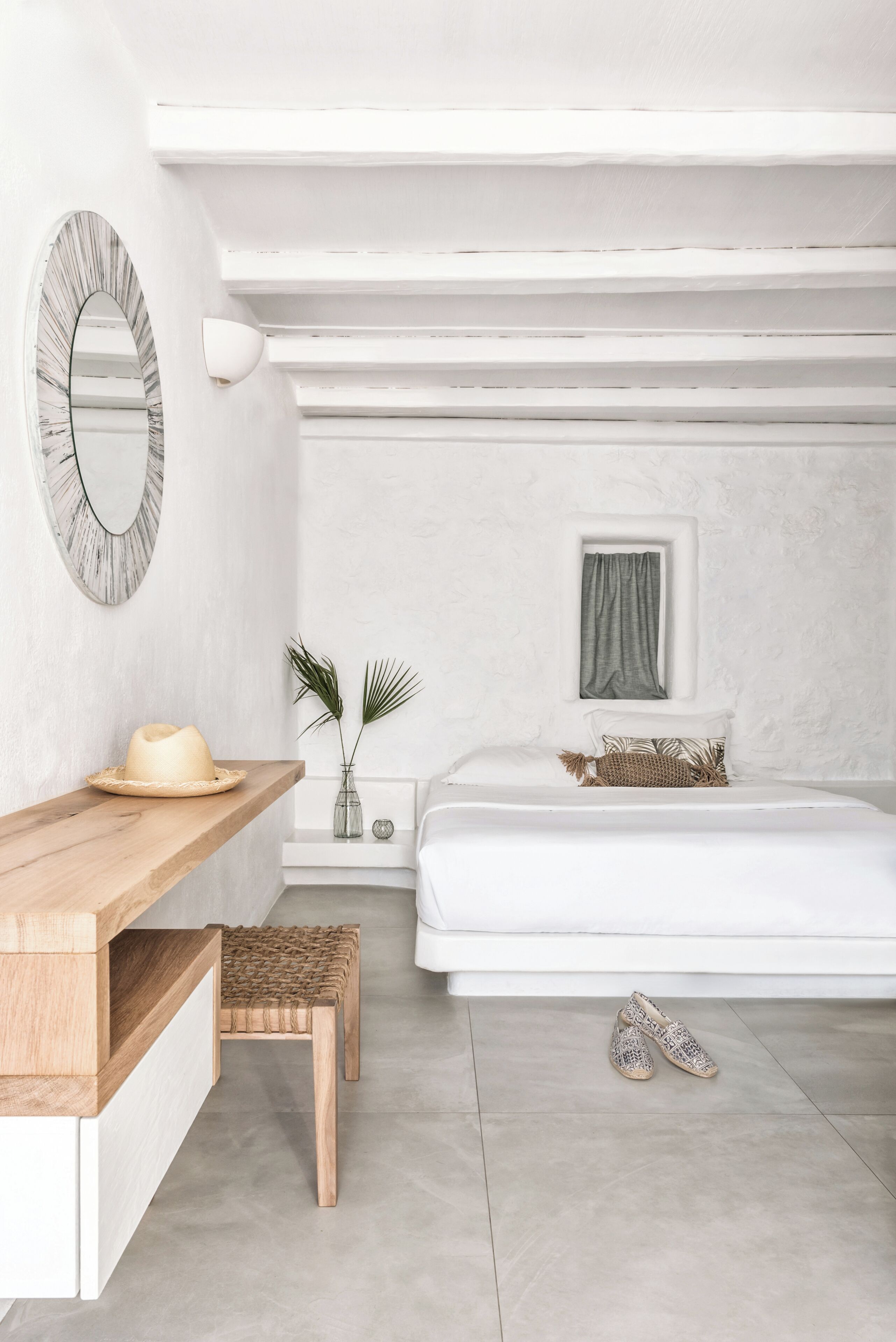 A bedroom with a bed, bedside table, mirror, and a small window.