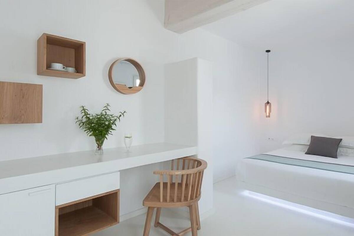 A minimalist bedroom with a bed, bedside table, chair, and a small shelf with cups.