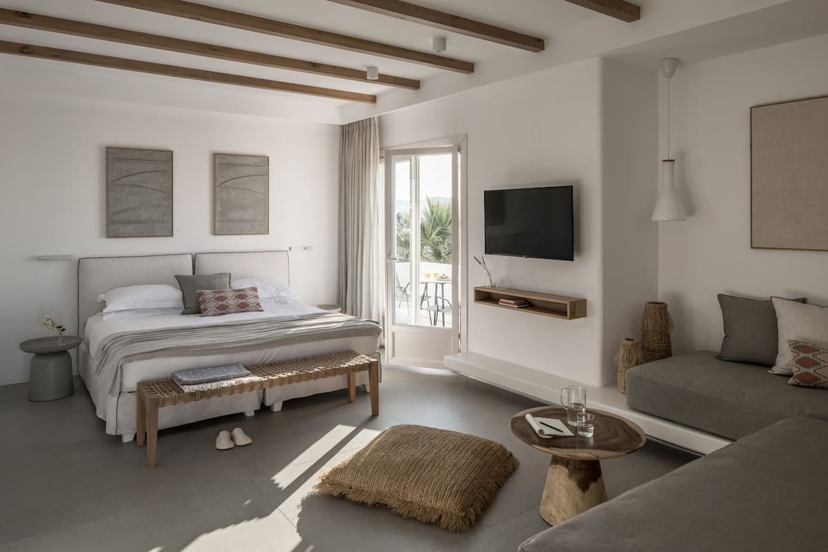 A modern bedroom with a bed, bench, sofa, and TV.