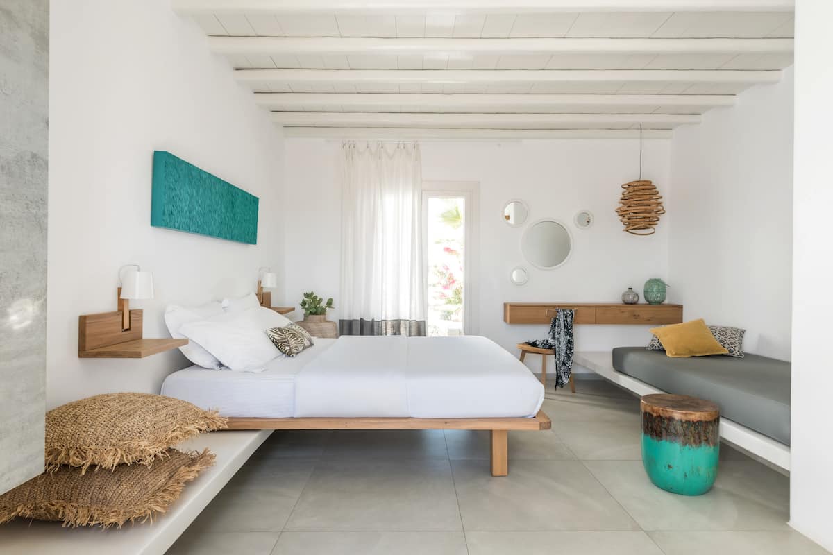 A modern bedroom with a bed, bedside tables, a bench, a sofa, and a round wooden stool.