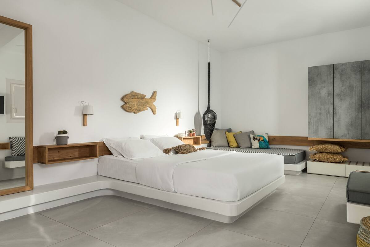 A modern bedroom with a large bed, bedside tables, a wall-mounted fish decoration, a hanging light, and a grey cabinet.
