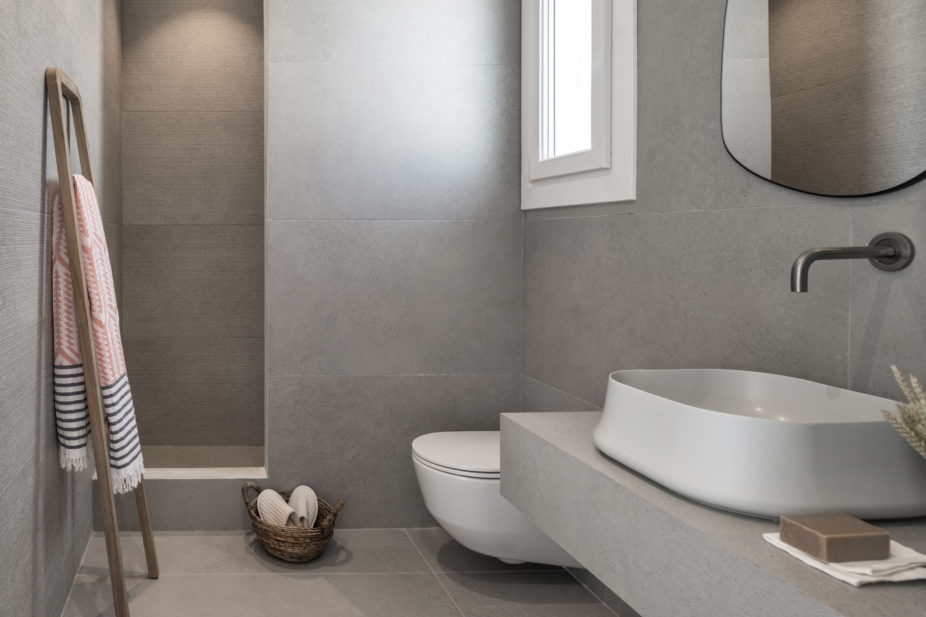 A modern bathroom with a large vessel sink, a toilet, a shower, and a towel rack with patterned towels.