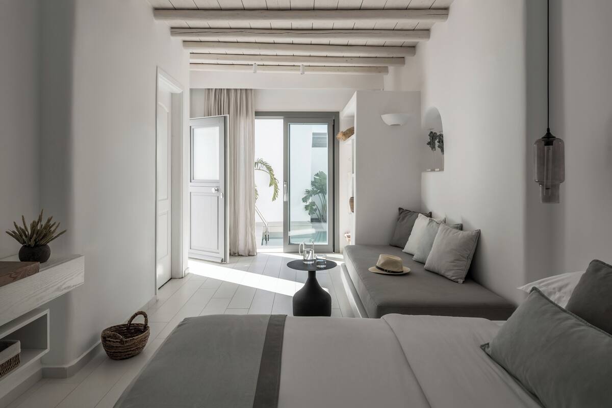 A modern hotel room with a bed, a sofa, a small table, and a view of the outdoors.