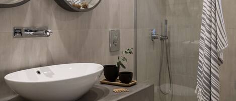 Un baño moderno con un lavamanos ovalado grande, dos espejos fijos en la pared, un box de ducha con paredes de vidrio y una toalla a rayas.