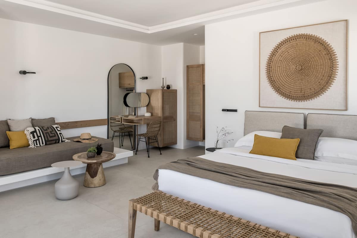 A modern hotel room with a bed, a sofa, a dining table, and a small seating area.
