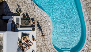 An aerial view of a pool area with stone flooring, lounge chairs, and a few people relaxing. - A Hotel Mykonos (Mykonos)