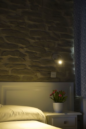 Un dormitorio con una pared con diseño de piedra, una mesita de noche con una planta en maceta y una mesita con una lámpara.