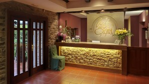 A reception area with a stone wall, a wooden reception desk, and a sign that reads "Welcome". - Izalde (Ayala)