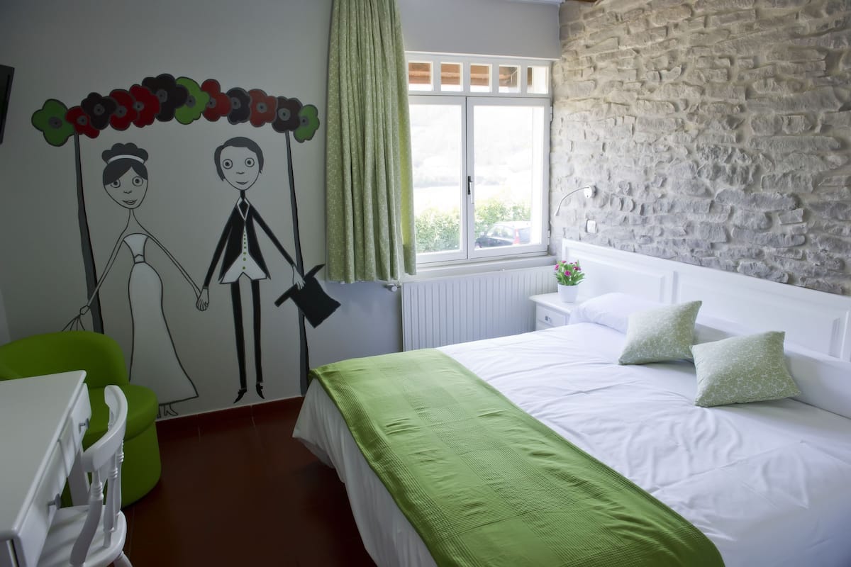 Un dormitorio con pared de piedra, una cama con ropa blanca, un sillón verde y un adorno mural de una pareja.