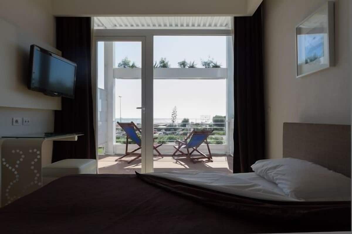 A hotel room with a bed, a TV, a desk, and a balcony with two chairs.