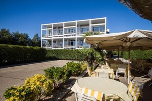A hotel with outdoor seating, a white building in the background, and a clear sky. - Hotel La Conchiglia (Fiumicino)