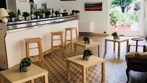 Un café con taburetes y mesas de madera, una barra con botellas, y plantas en macetas.