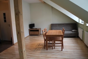 A room with a wooden dining table, chairs, a grey sofa, a TV on a wooden stand, and a window with a view. - 999 Aparthostel (Kraków)
