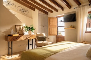 A bedroom with a bed, a desk, a chair, a TV, and a window with curtains.