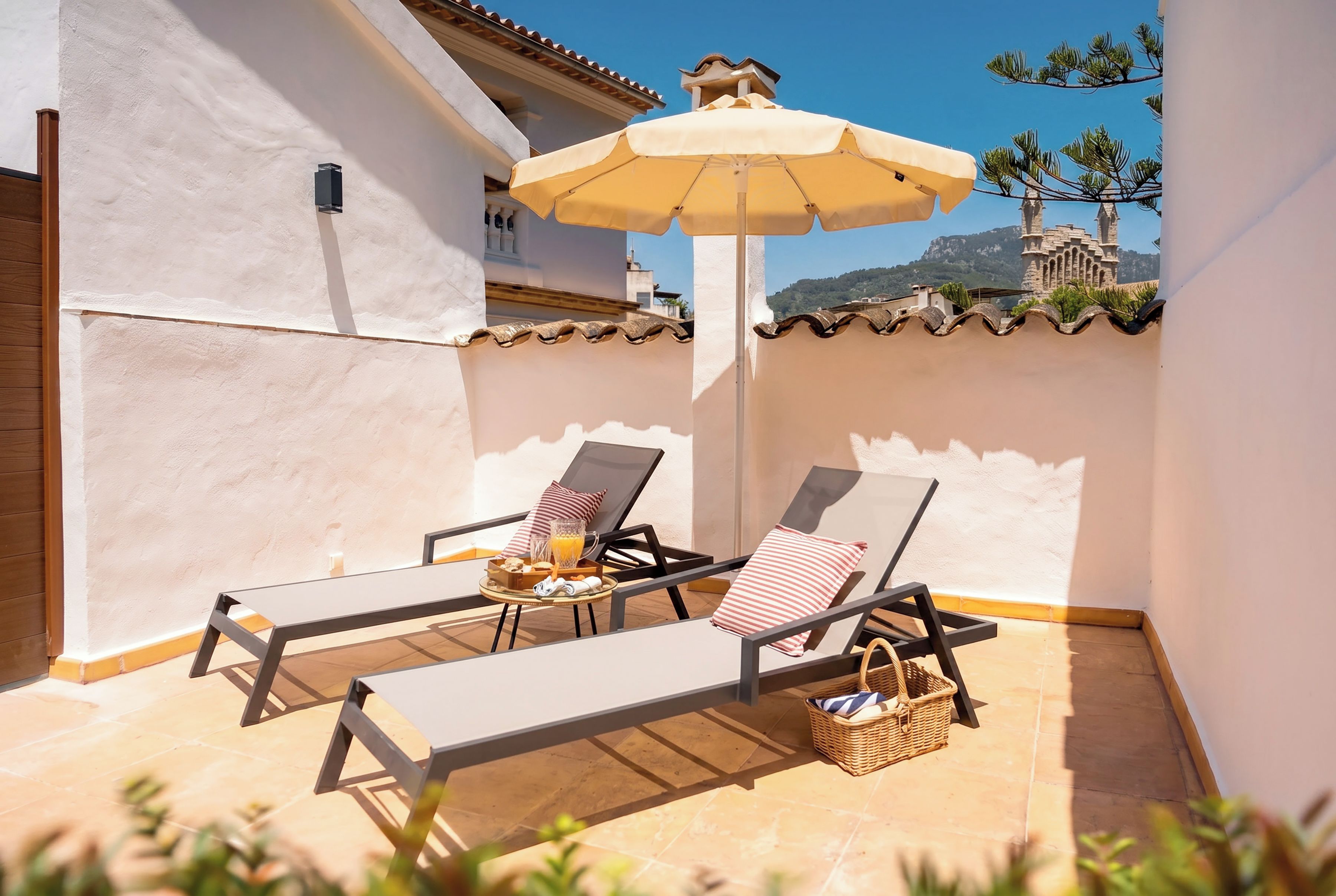 A sunlit patio with two lounge chairs, a table with a tray of food, and a large umbrella.