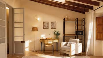 A room with a wooden ceiling, a white chair, a desk with a lamp, and a bookshelf.