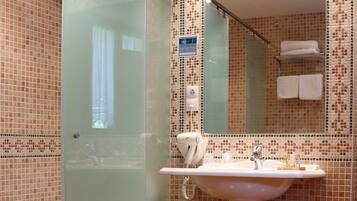 Un baño con cabina de ducha de vidrio, un lavabo con espejo y un taburete pequeño.