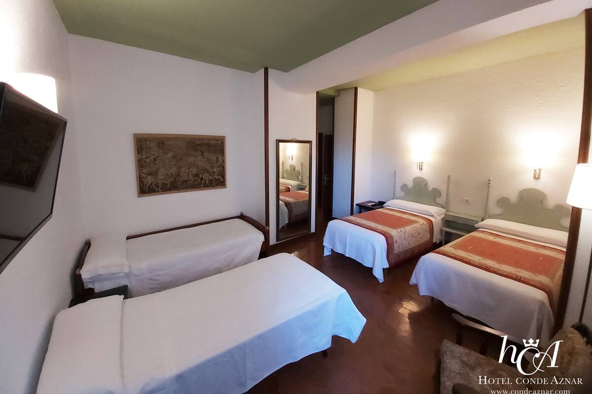 A hotel room with three single beds, a wooden headboard, a mirror, and a painting on the wall.
