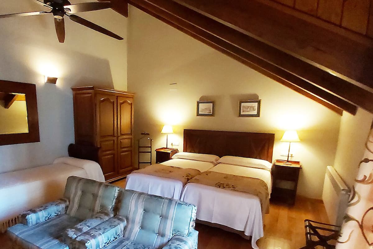 A bedroom with a bed, a sofa, a wooden wardrobe, and a ceiling fan.