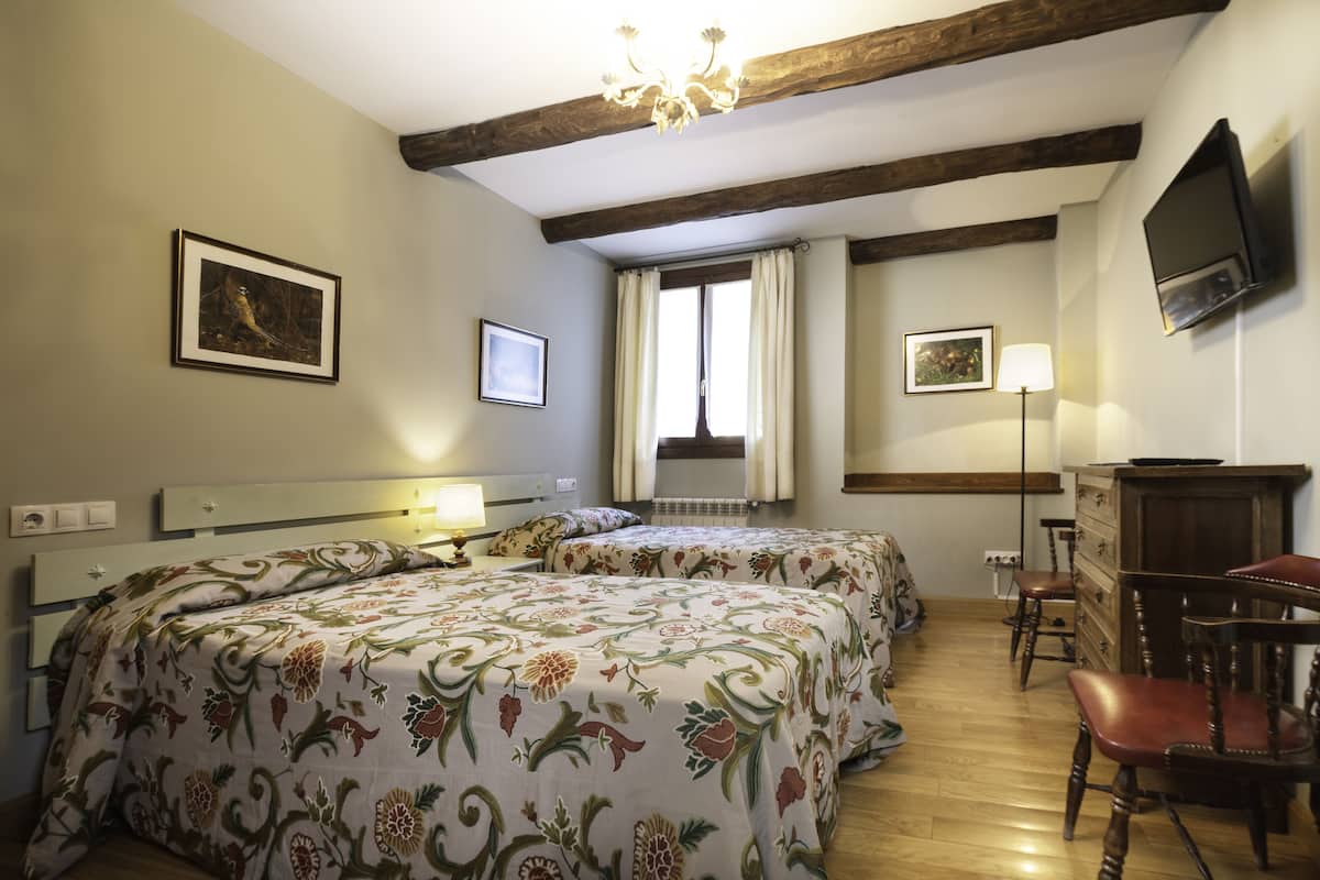 A bedroom with two beds, a dresser, a TV, and a window with curtains.