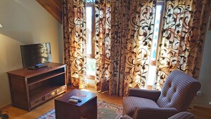 A living room with a television on a wooden stand, a coffee table, a striped armchair, and curtains with a floral pattern. - Conde Aznar (Jaca)