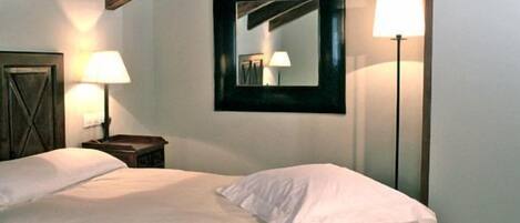 A bedroom with a bed, two bedside lamps, a mirror, and a wooden ceiling beam.
