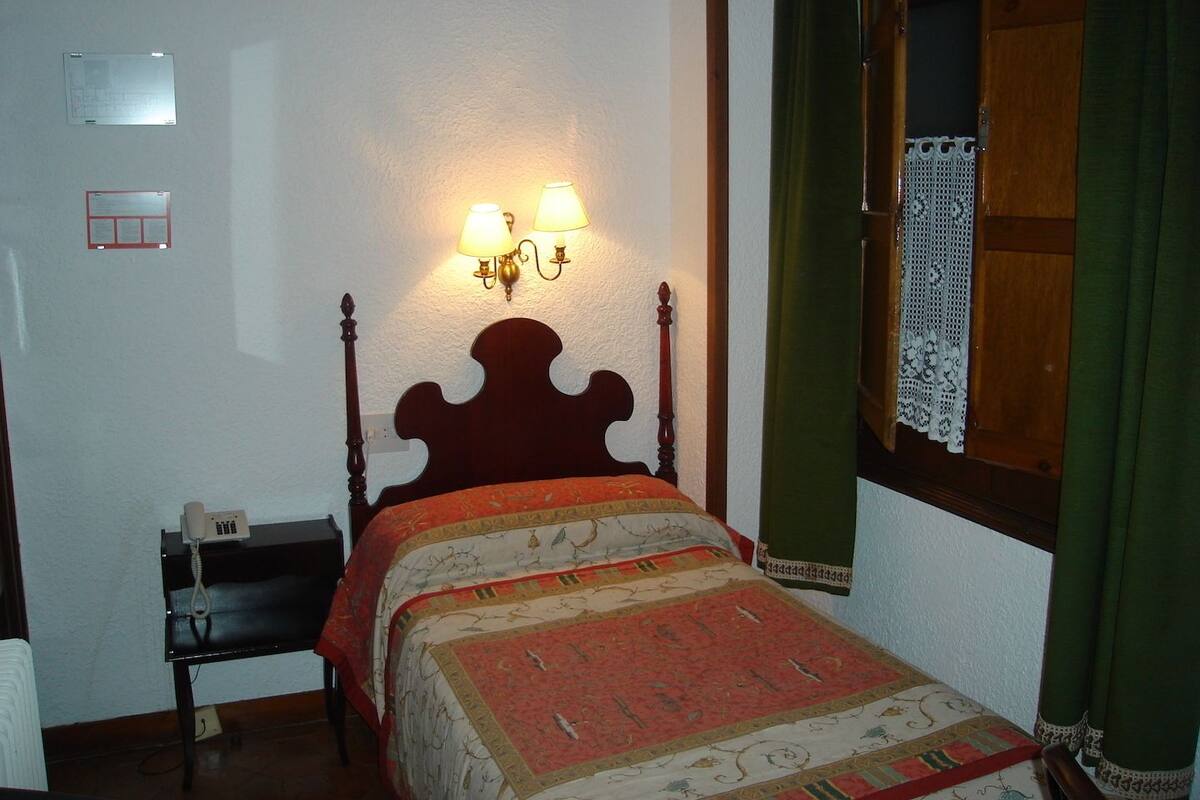A room with a bed, a bedside table with a telephone, and a wall-mounted lamp.