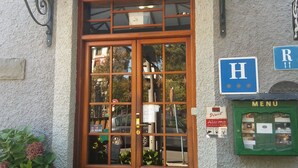 A wooden double door with glass panels, a green mailbox, and a blue sign with an 'H' and 'R' indicating hotel and restaurant. - Conde Aznar (Jaca)