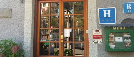 A wooden double door with glass panels, a green mailbox, and a blue sign with an 'H' and 'R' indicating hotel and restaurant.