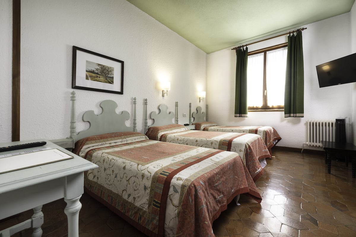 A hotel room with two beds, a desk, a television, and a window with curtains.