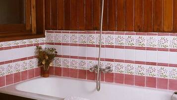 Un baño con tocador de madera, bañera blanca y salpicadero de azulejos con motivos florales.