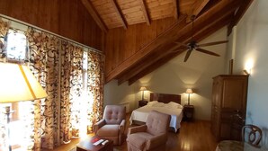 A cozy room with wooden beams, a ceiling fan, two bedside lamps, a bed, and a chair. - Conde Aznar (Jaca)