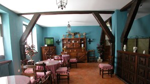 A dining area with wooden tables and chairs, a television, and a bookshelf with decorative items. - Conde Aznar (Jaca)