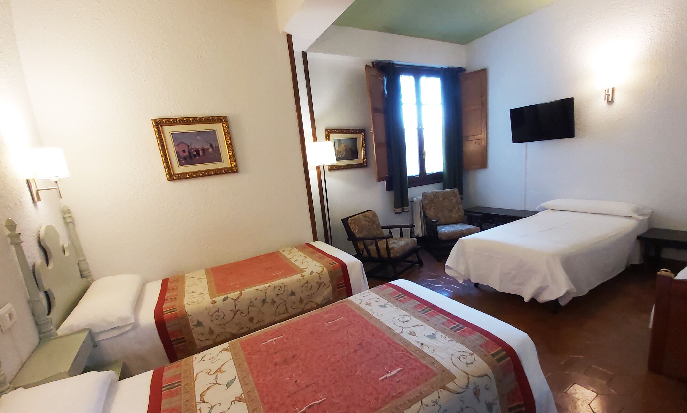 Habitación de hotel con dos camas, una silla, un escritorio, un televisor y dos cuadros en la pared.