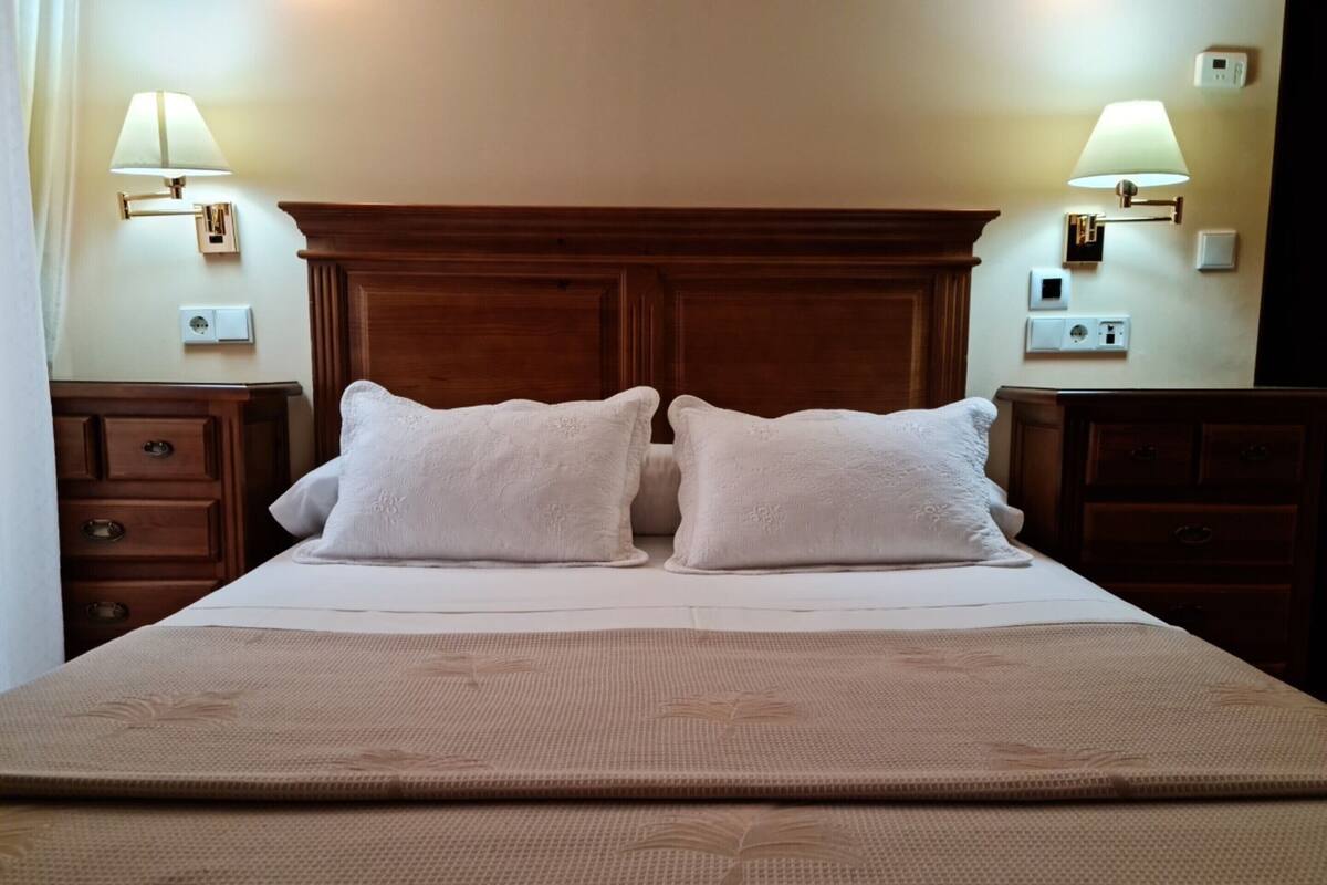 A neatly made bed with two pillows, a wooden headboard, and two bedside tables with lamps.