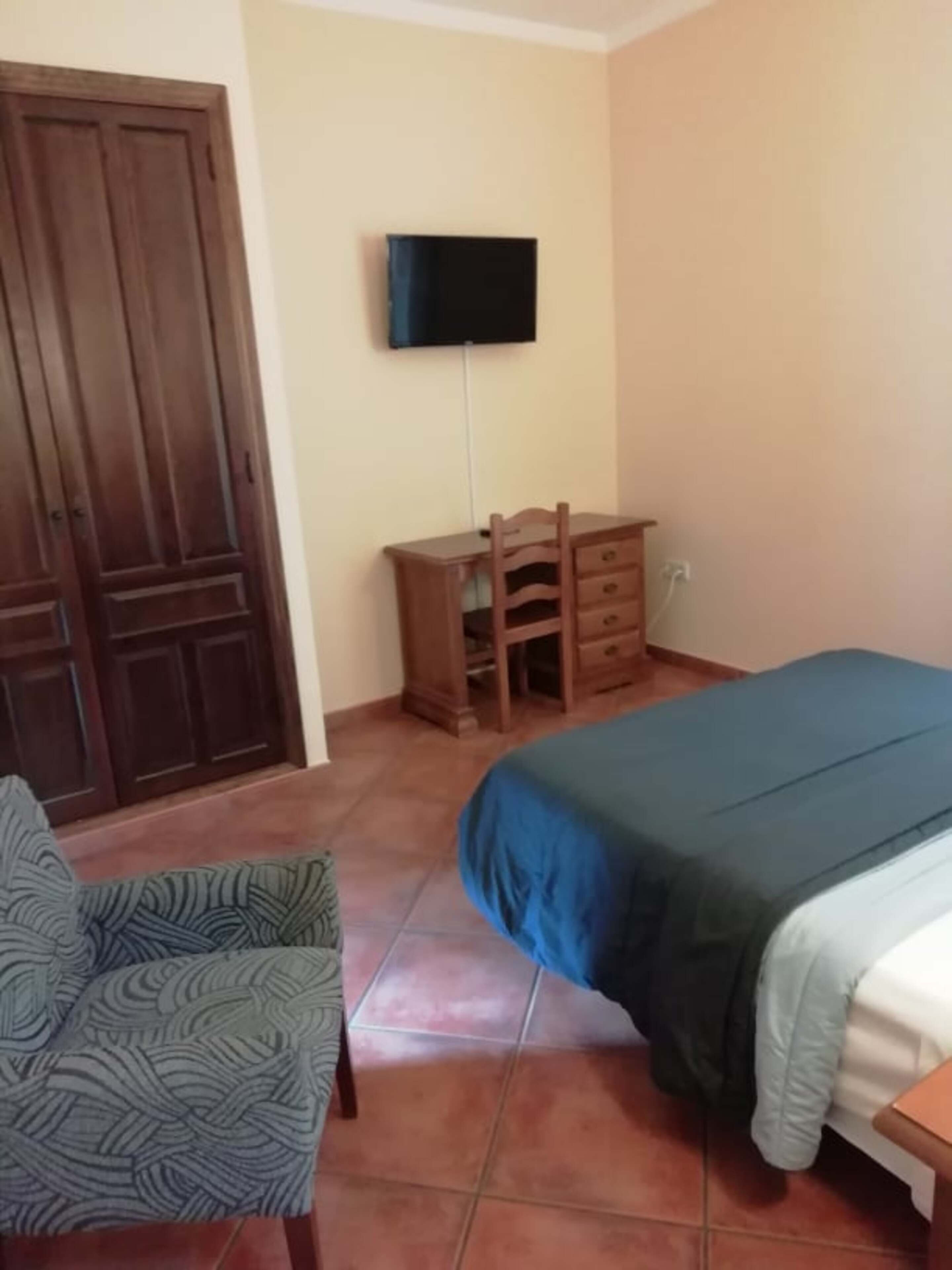 A bedroom with a bed, a desk, a chair, and a TV mounted on the wall.