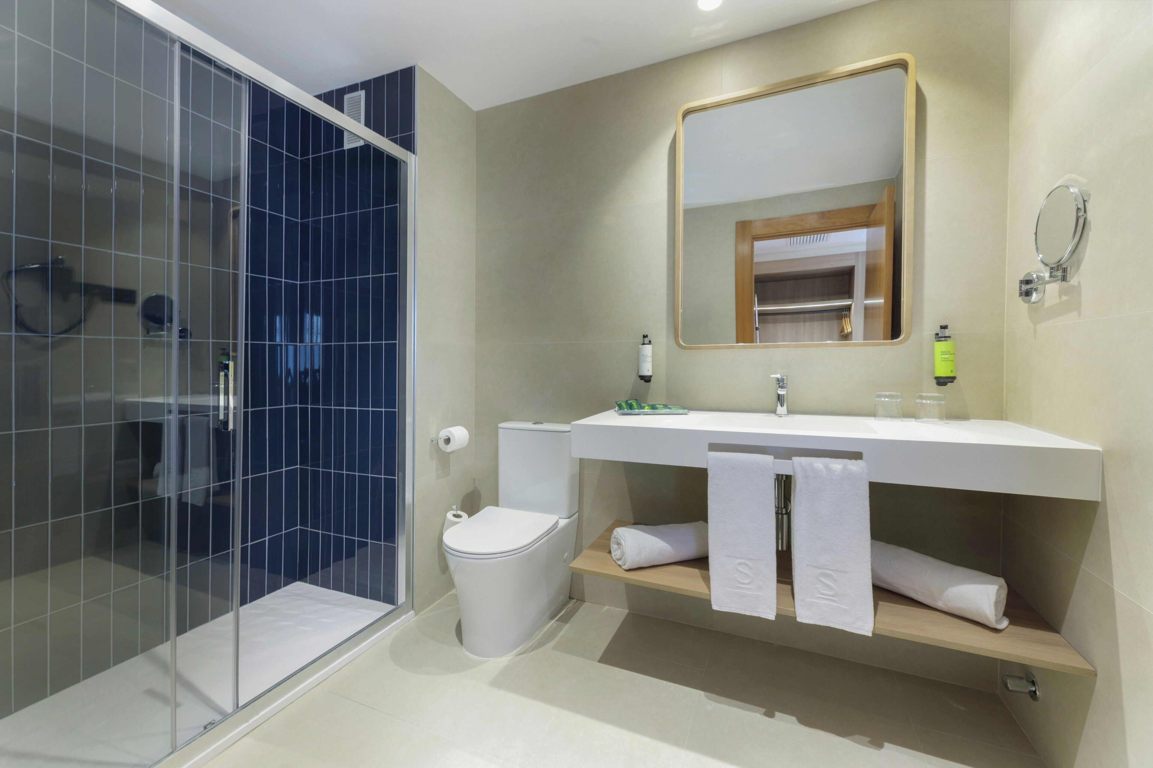 A modern bathroom with a glass shower enclosure, a toilet, a sink with a mirror, and a towel rack.