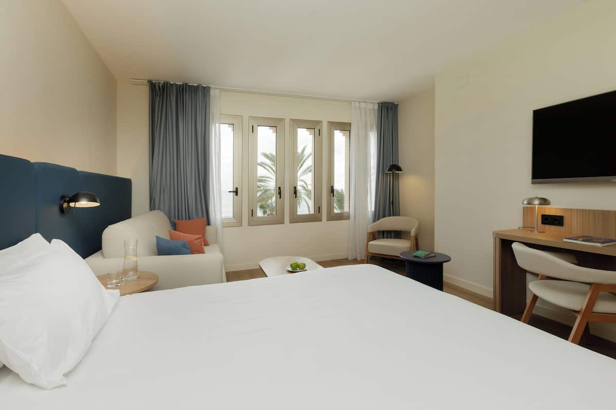 A hotel room with a large bed, a desk, a chair, a TV, and a window with curtains.